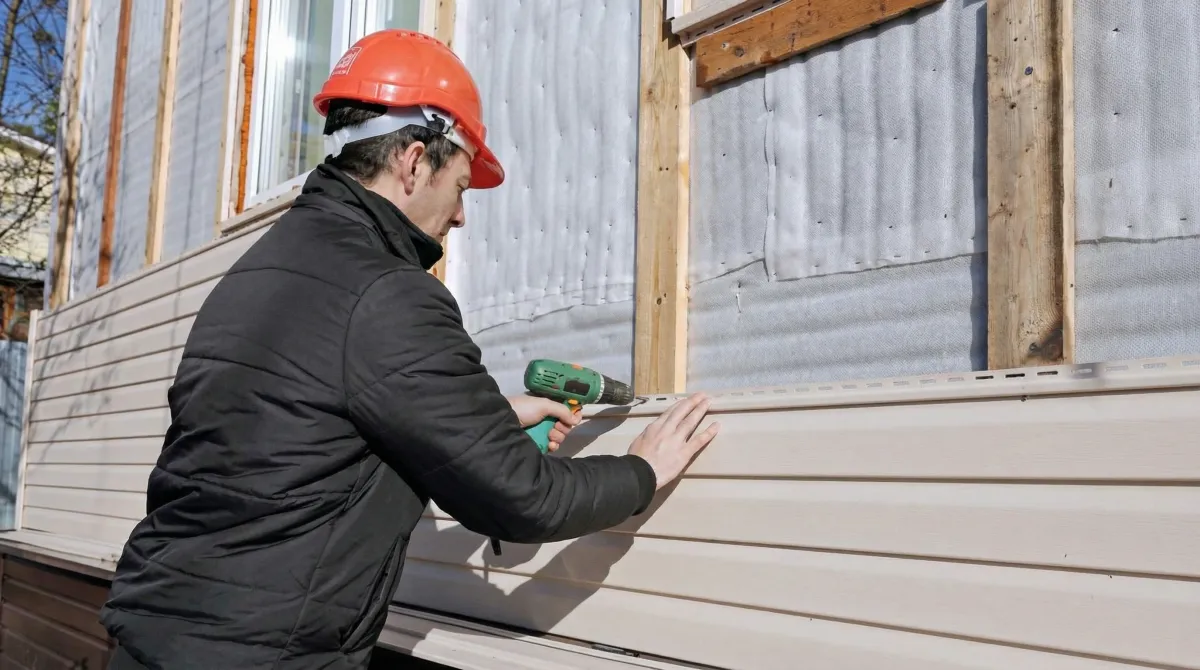 Siding replacement professional using a power drill to install new tan vinyl siding on a home exterior in Miami, FL